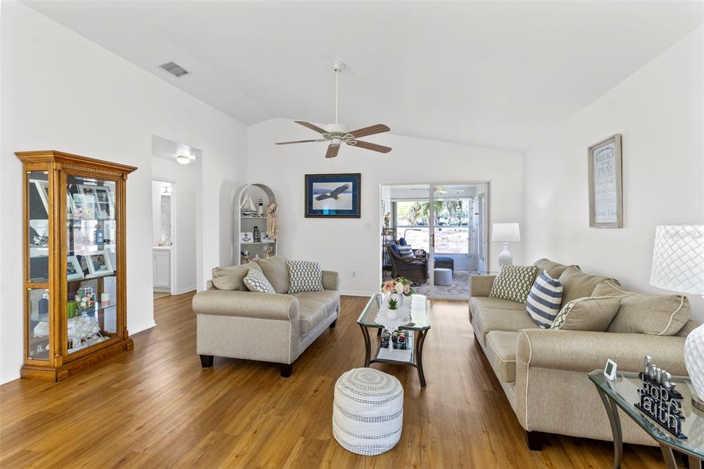 A living room features light-colored sofas, a glass coffee table, and wood-look flooring — 4960 HERON RUN CIRCLE, LEESBURG, FL