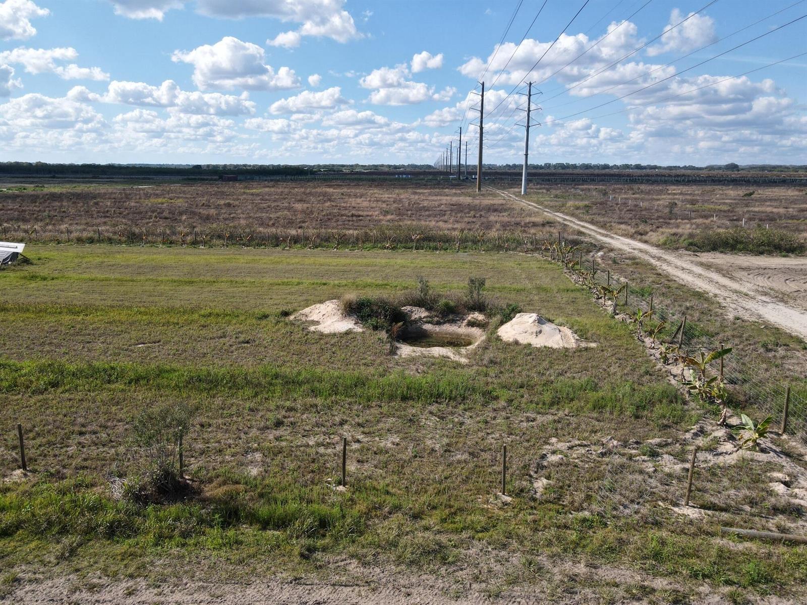 An aerial view of a grassy field featuring a small pond and utility power lines — 6694 5th Road, FL 33935, FL