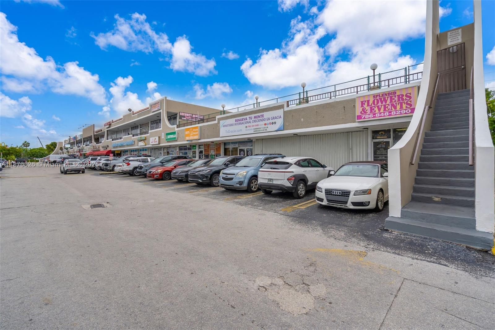 An exterior view of a commercial strip mall with parked cars and an outdoor staircase — 7147 SW 8th St, Miami FL 33144, MIAMI, FL
