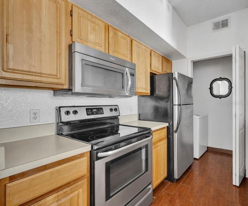 A kitchen features light wood cabinets, stainless steel appliances, and dark wood-look flooring — 13003 PLANTATION PARK CIRCLE UNIT 1319, ORLANDO, FL