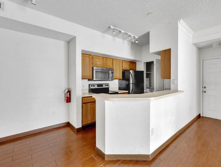 A kitchen with wood cabinets, black appliances, and a breakfast bar overlooking a living area — 13003 PLANTATION PARK CIRCLE UNIT 1319, ORLANDO, FL