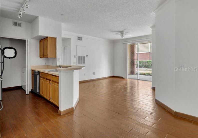 An open-concept kitchen with wood cabinets and a breakfast bar overlooks a living area — 13003 PLANTATION PARK CIRCLE UNIT 1319, ORLANDO, FL