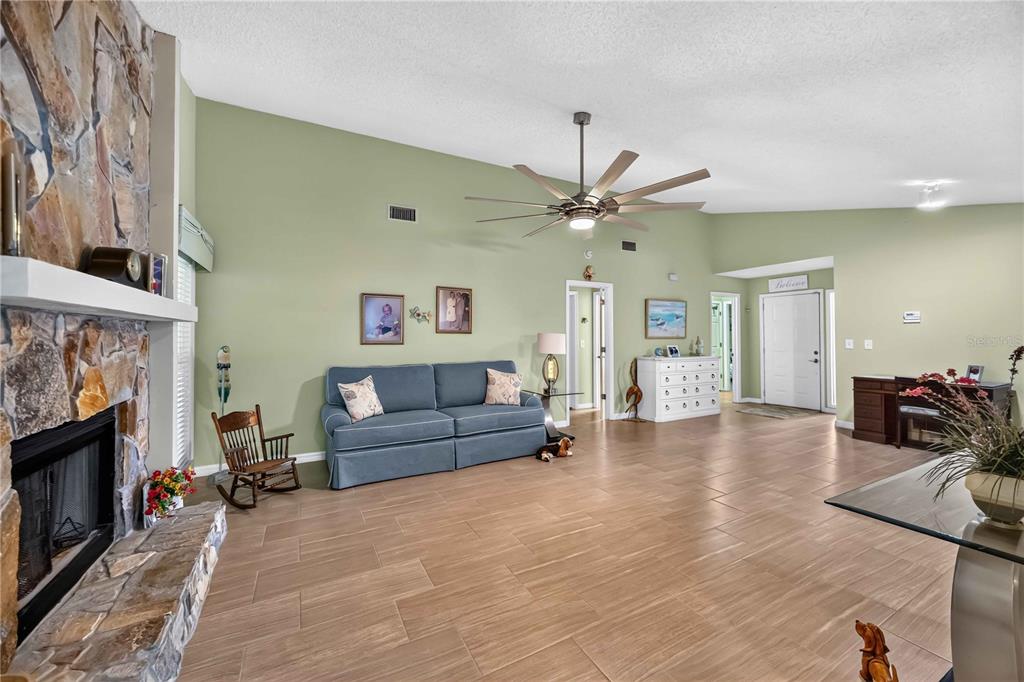 A living room with a stone fireplace, blue sofa, ceiling fan, and light-colored tile floors — 3505 45TH STREET W, BRADENTON, FL