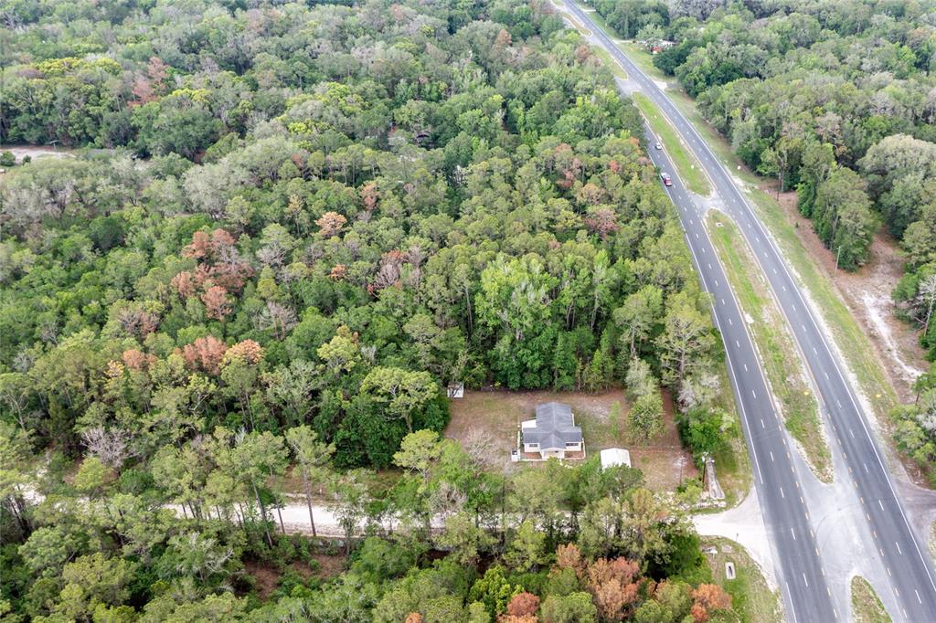 An aerial view shows a single-story house surrounded by dense forest next to a highway — 16913 NE 77TH LANE, HAWTHORNE, FL