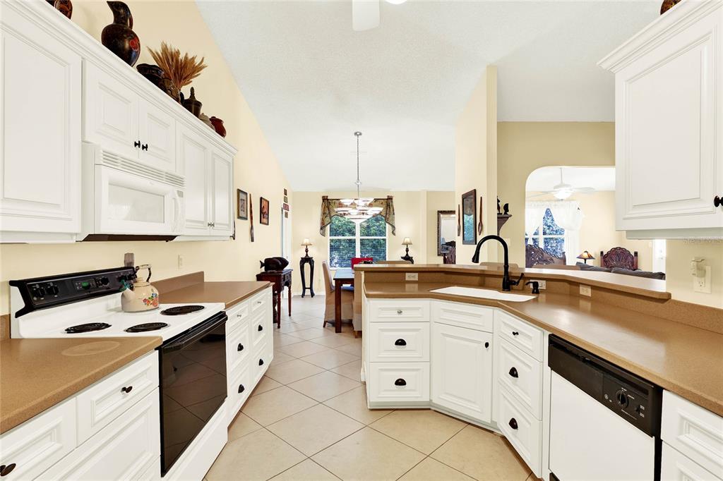 A kitchen with white cabinets, tan countertops, and tile flooring opens into a dining area — 4721 TARA VIEW ROAD, LEESBURG, FL