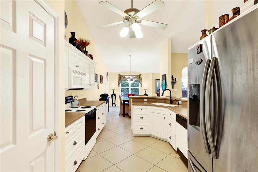 A kitchen with white cabinets, stainless steel appliances, and tile flooring leads to a dining area — 4721 TARA VIEW ROAD, LEESBURG, FL