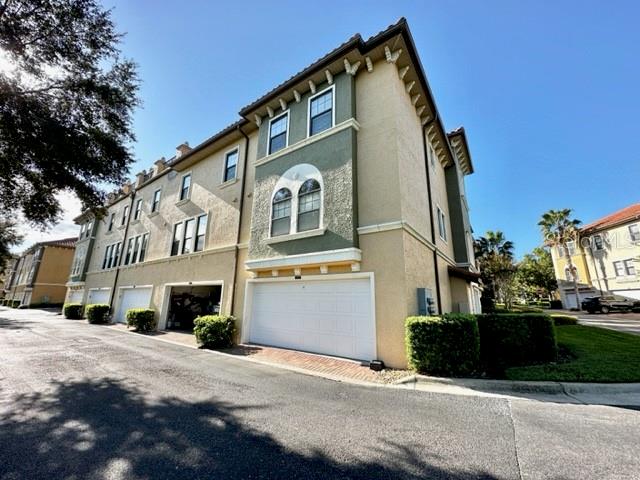 A multi-story townhouse exterior features tan stucco walls, green accents, and ground-level garage doors — 4232 MESSINA DRIVE, LAKE MARY, FL