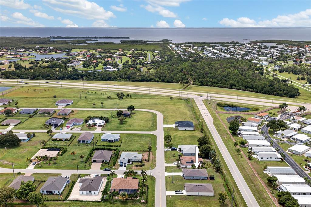 An aerial view shows a suburban neighborhood with houses, roads, and a distant body of water — 25138 ALICANTE DRIVE, PUNTA GORDA, FL