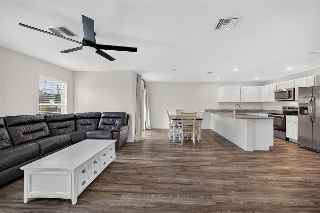 An open-concept living room and kitchen with wood-look flooring, a black sectional, and white cabinetry — 25138 ALICANTE DRIVE, PUNTA GORDA, FL