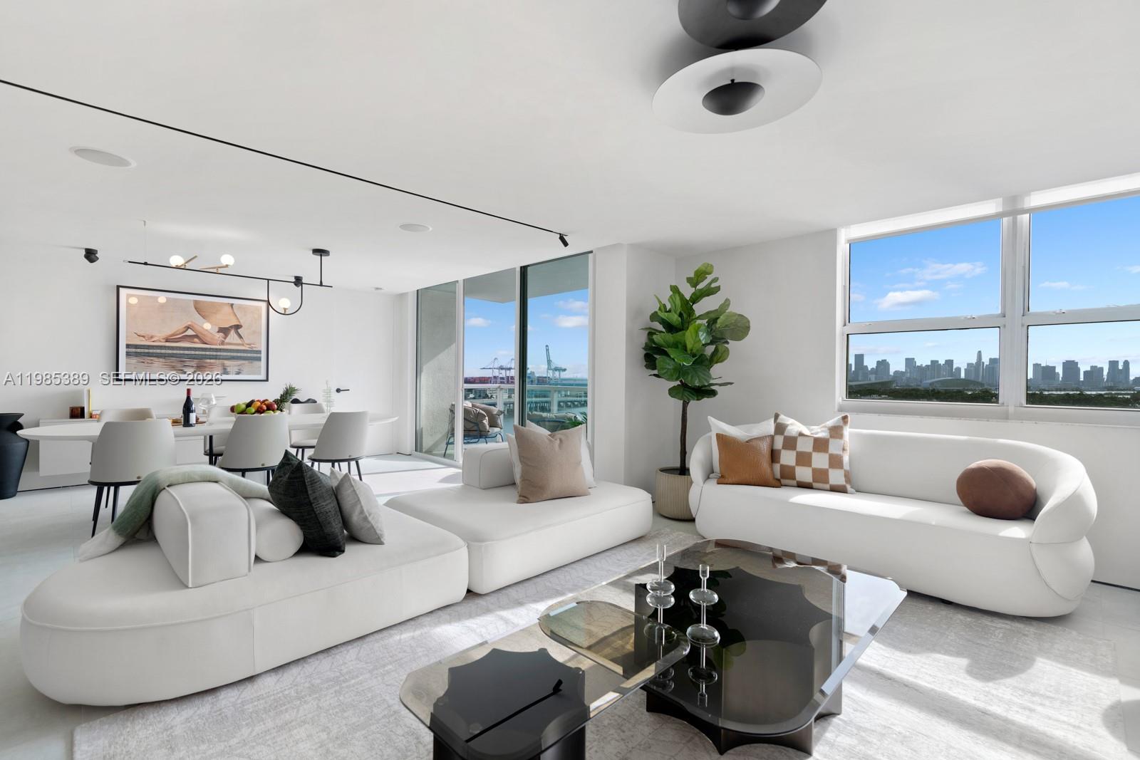 A modern living and dining area features white sofas, a glass coffee table, and city views — 650 West Ave, Miami Beach FL 33139, MIAMI BEACH, FL