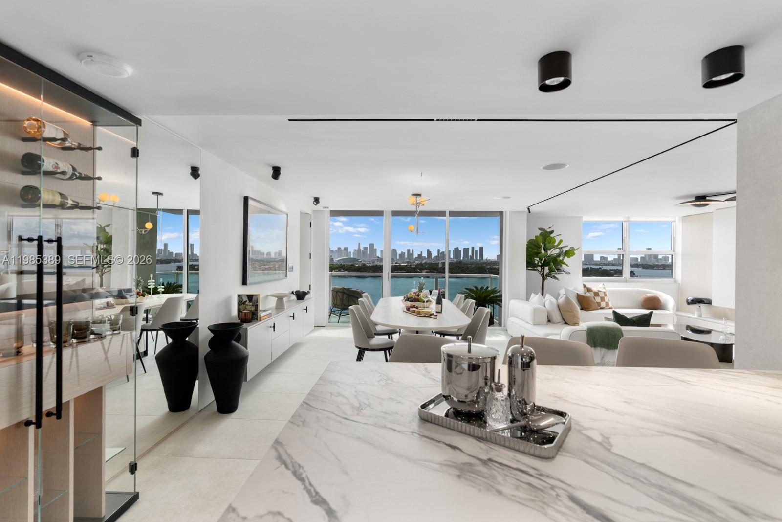 A modern open-concept living and dining area features marble surfaces, a wine display, and waterfront views — 650 West Ave, Miami Beach FL 33139, MIAMI BEACH, FL