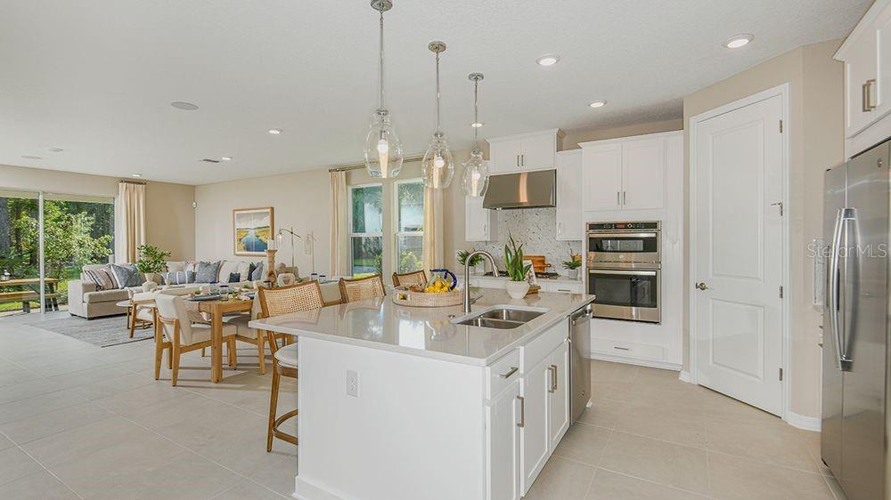 A bright, open-concept kitchen features white cabinetry, quartz countertops, a center island, and stainless appliances — 4 ARMENIA COURT, PALM COAST, FL