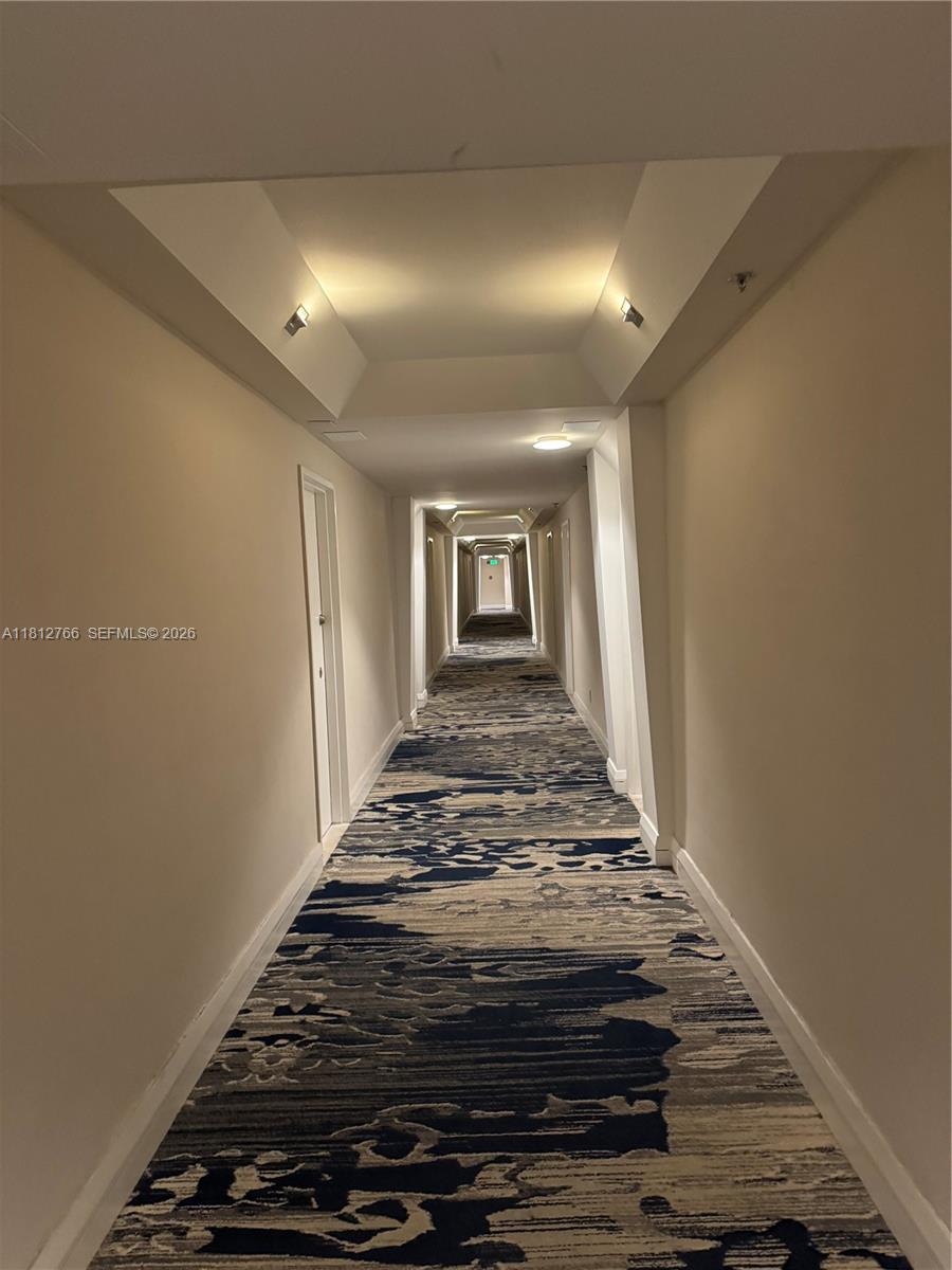 A long hotel hallway features beige walls, recessed lighting, and a patterned blue and gray carpet — 5161 Collins Ave # 315, Miami Beach FL 33140, MIAMI BEACH, FL