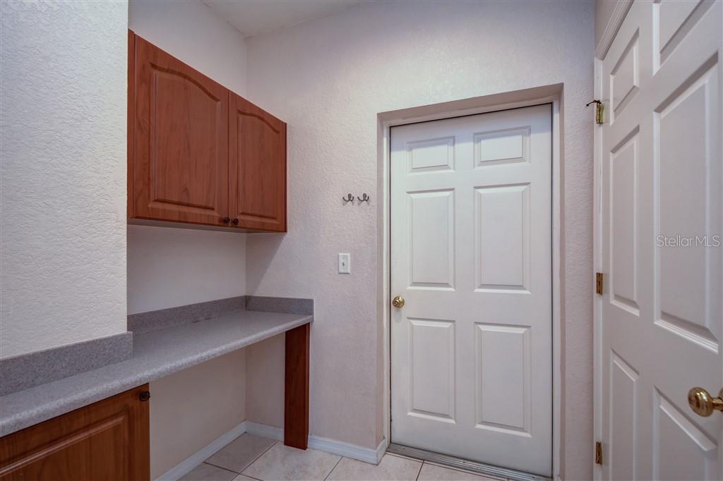 A laundry room features wood cabinets, a gray countertop, and a white door — 1812 BAYSHORE WAY, CLEARWATER, FL