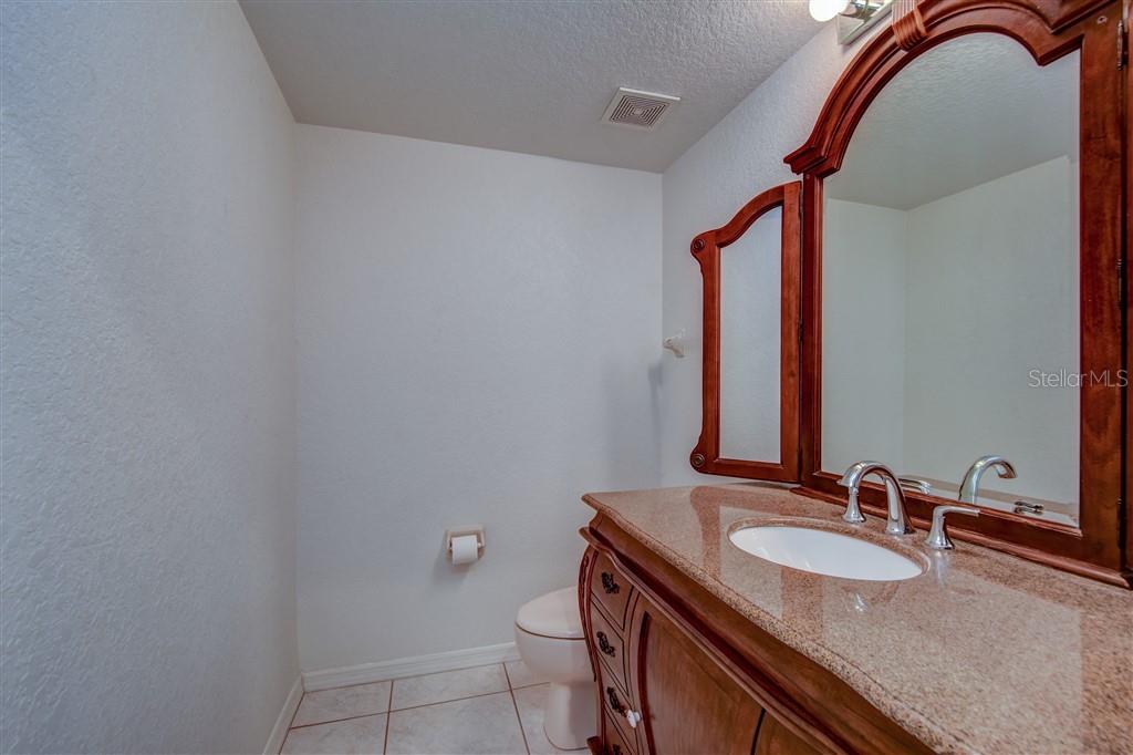 A bathroom features a wooden vanity with a granite countertop and a decorative mirror — 1812 BAYSHORE WAY, CLEARWATER, FL