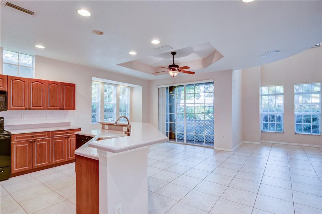 A kitchen with wood cabinets, a breakfast bar, and tile flooring opens to a living area — 1812 BAYSHORE WAY, CLEARWATER, FL
