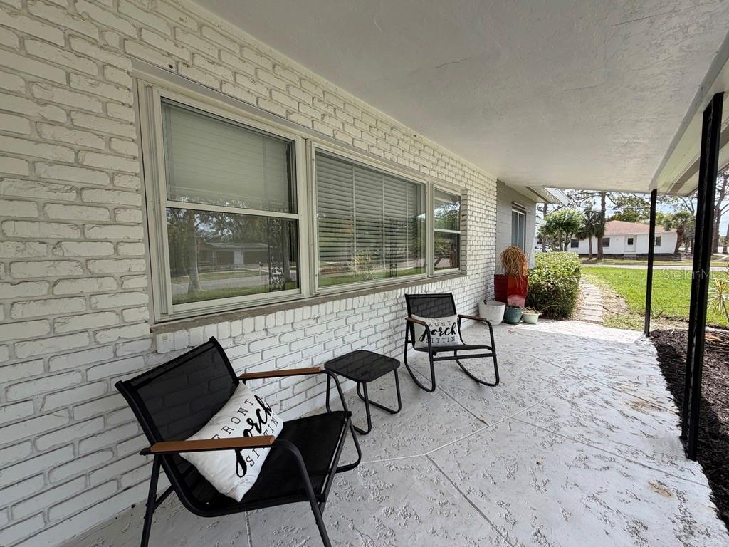 A covered porch with white brick walls, two black chairs, and a small side table — 361 SCOTT AVENUE, SARASOTA, FL