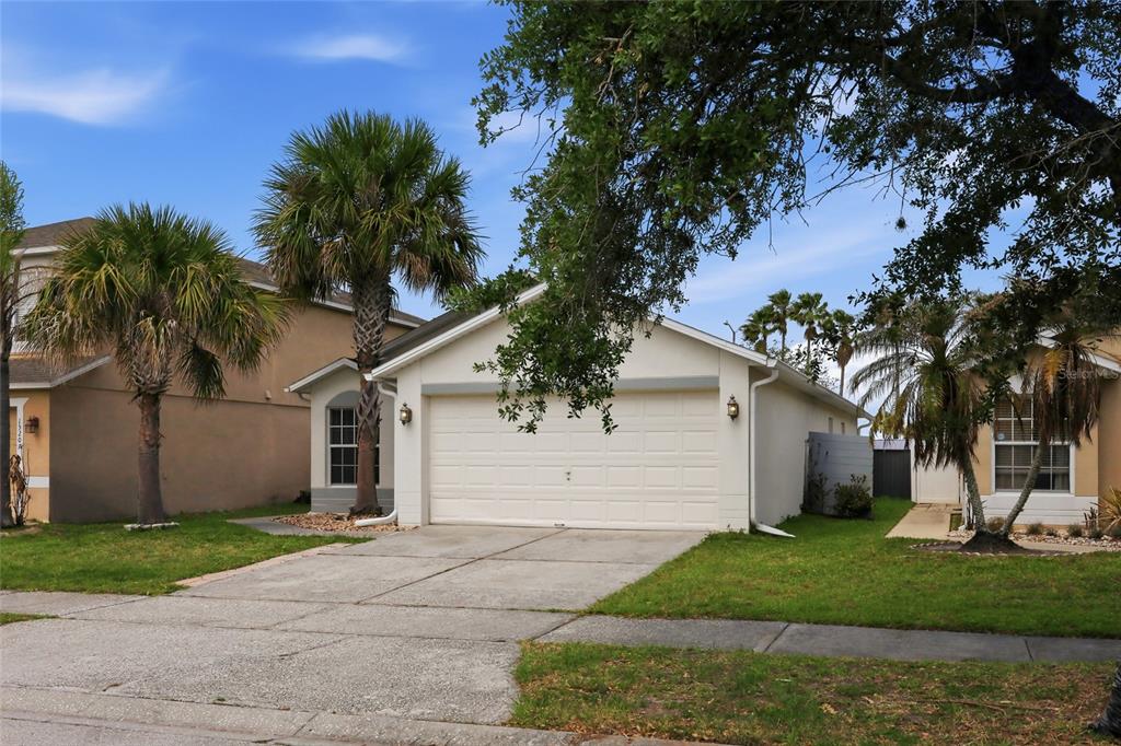 A single-story house with a white garage door, a concrete driveway, and palm trees — 15187 HARROWGATE WAY, WINTER GARDEN, FL