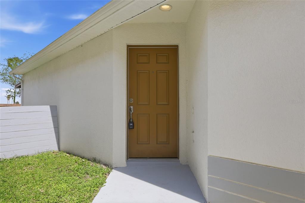 A brown front door is set into a beige stucco exterior wall with a walkway — 15187 HARROWGATE WAY, WINTER GARDEN, FL