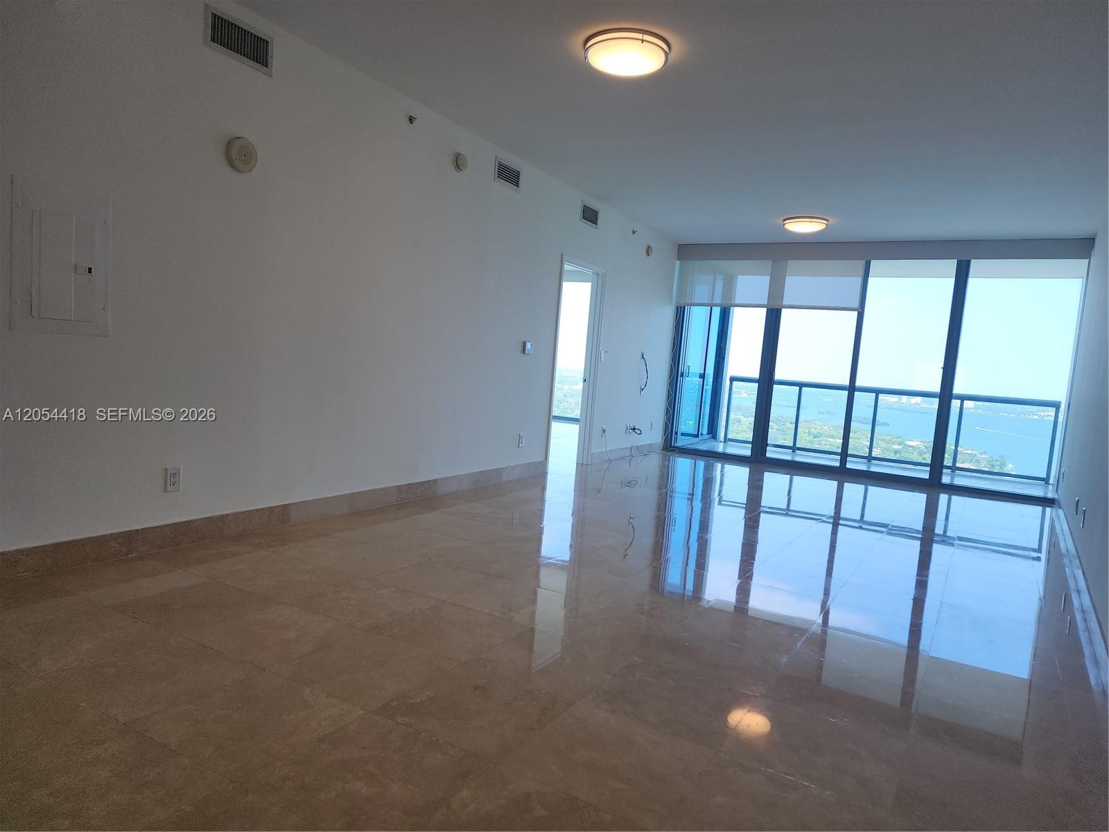 An empty room features polished tile floors, white walls, and floor-to-ceiling windows overlooking water — 601 NE 36th St # 3210, Miami FL 33137, MIAMI, FL