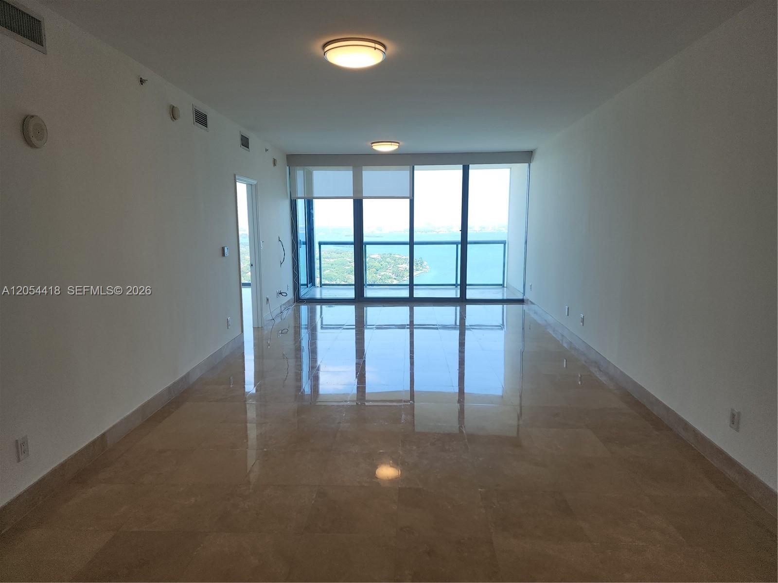 An empty room with polished tile floors, white walls, and floor-to-ceiling windows overlooking water — 601 NE 36th St # 3210, Miami FL 33137, MIAMI, FL