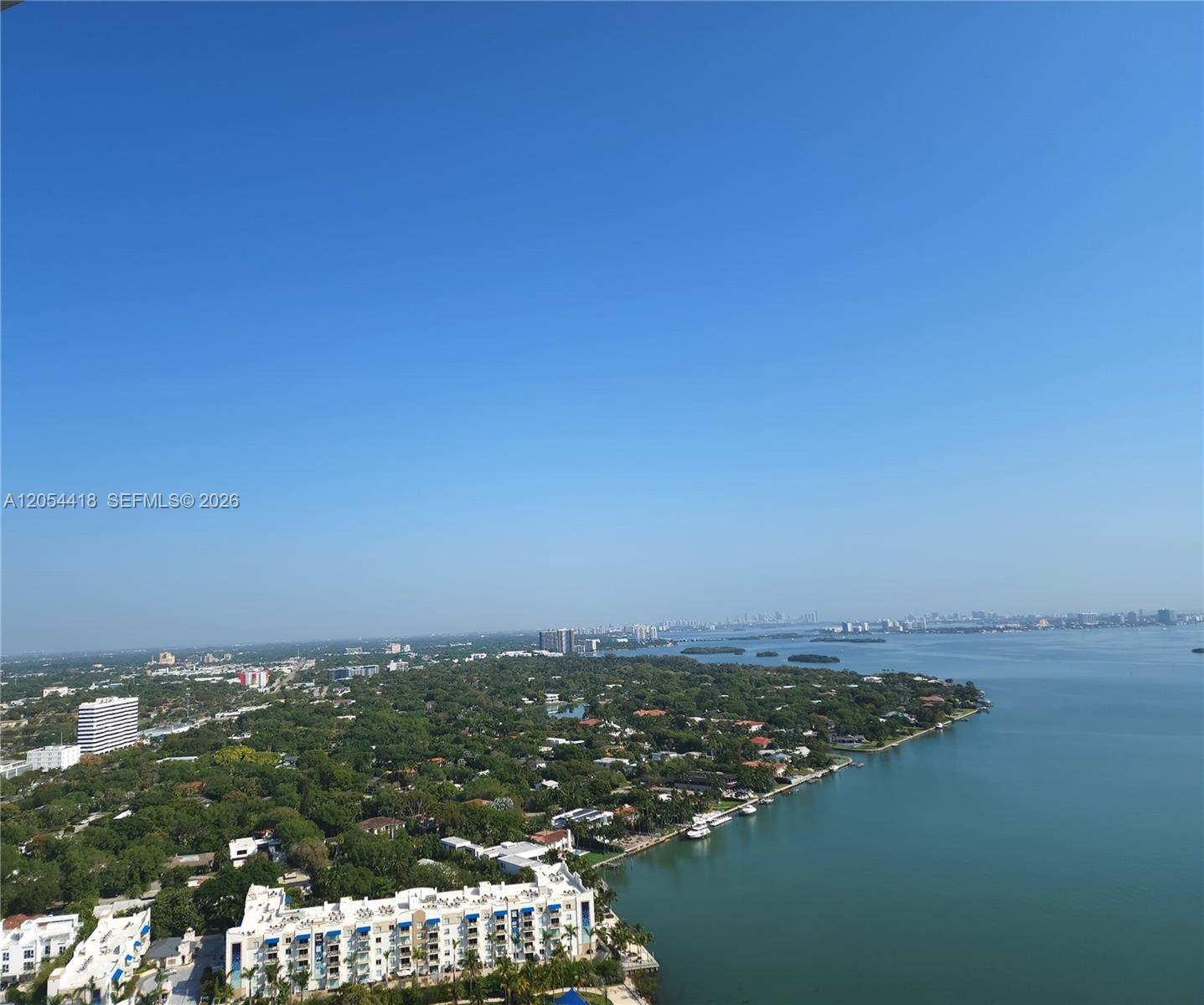 An aerial view shows a coastal residential area with buildings, lush trees, and a bay — 601 NE 36th St # 3210, Miami FL 33137, MIAMI, FL