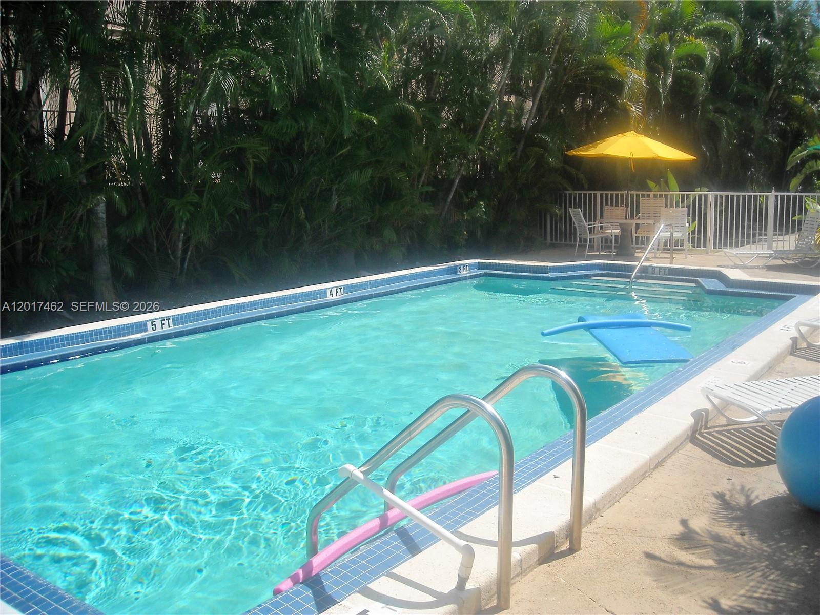 An outdoor swimming pool with a yellow umbrella and lounge chairs on the patio — 325 Fernwood Rd # 10, Key Biscayne FL 33149, KEY BISCAYNE, FL