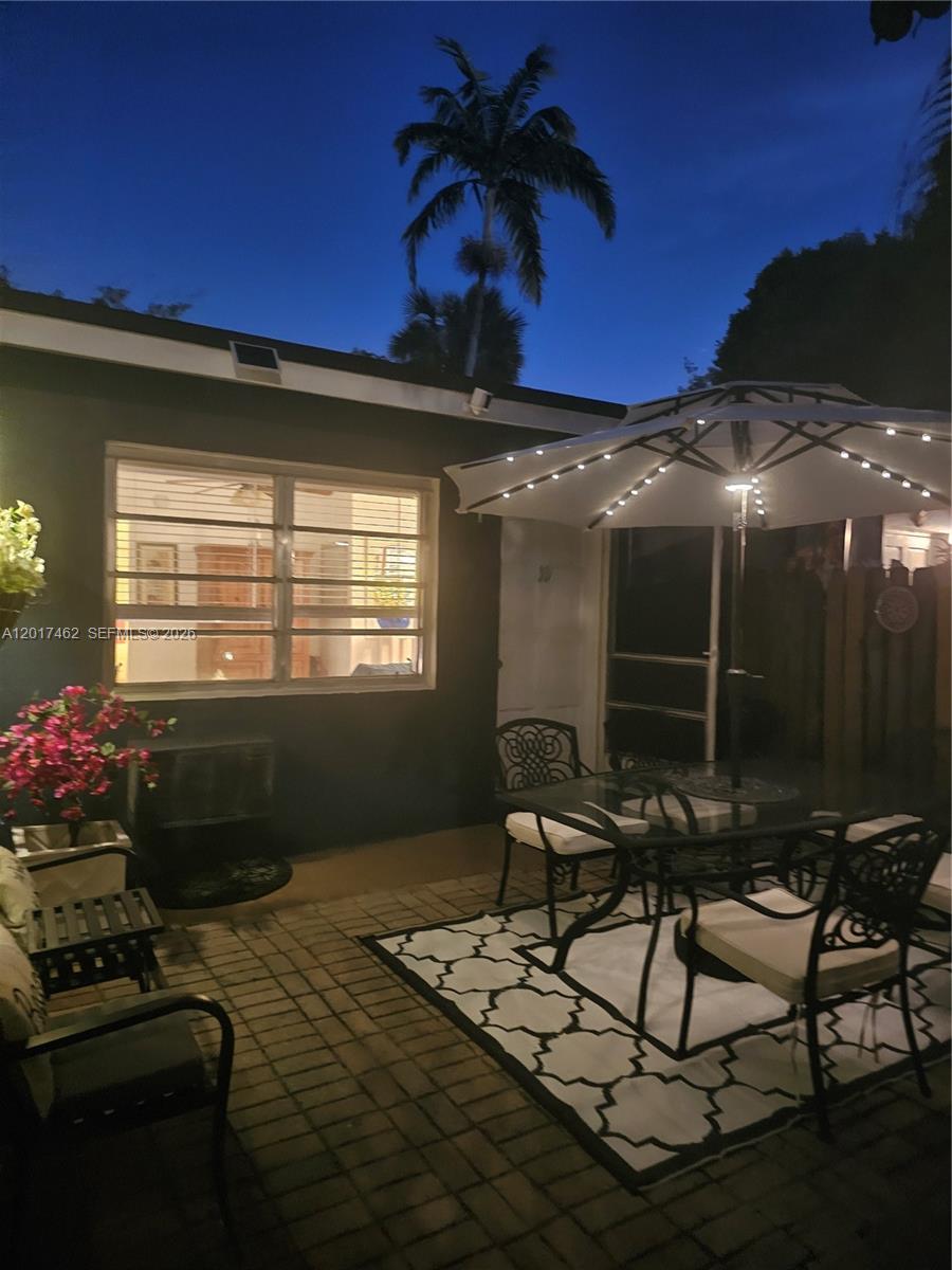 A paved patio features a dining set under an umbrella with string lights at dusk — 325 Fernwood Rd # 10, Key Biscayne FL 33149, KEY BISCAYNE, FL