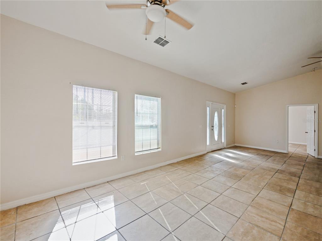 An empty living room features beige tile flooring, a ceiling fan, and two windows — 4901 BALBOA DRIVE, ORLANDO, FL