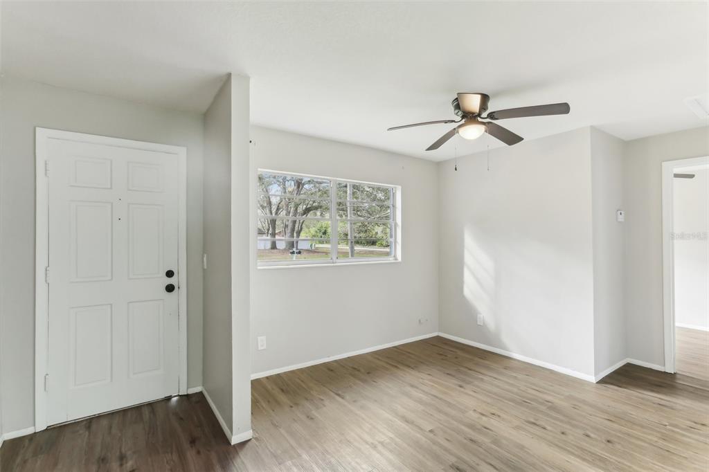 An empty room with light gray walls, wood-look flooring, a ceiling fan, and a window — 7711 AMHERST STREET, TAMPA, FL
