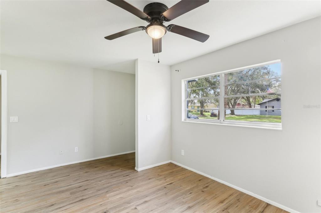 A bedroom with light gray walls, wood-look flooring, a ceiling fan, and a large window — 7711 AMHERST STREET, TAMPA, FL