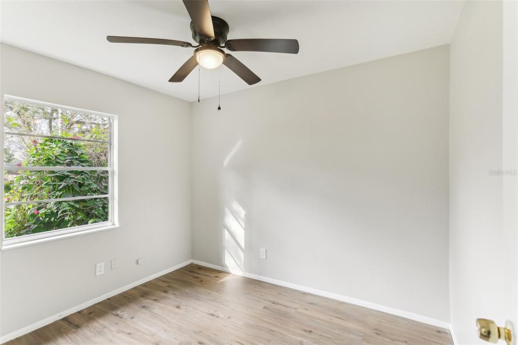 An empty bedroom features light-colored walls, wood-look flooring, a ceiling fan, and a window — 7711 AMHERST STREET, TAMPA, FL