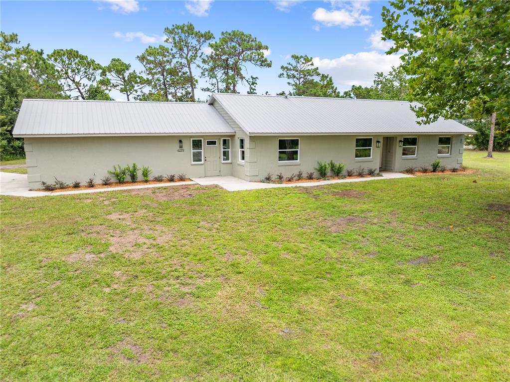 A single-story house with a light green exterior and a metal roof sits on grass — 4279 HENRY J AVE, ST CLOUD, FL