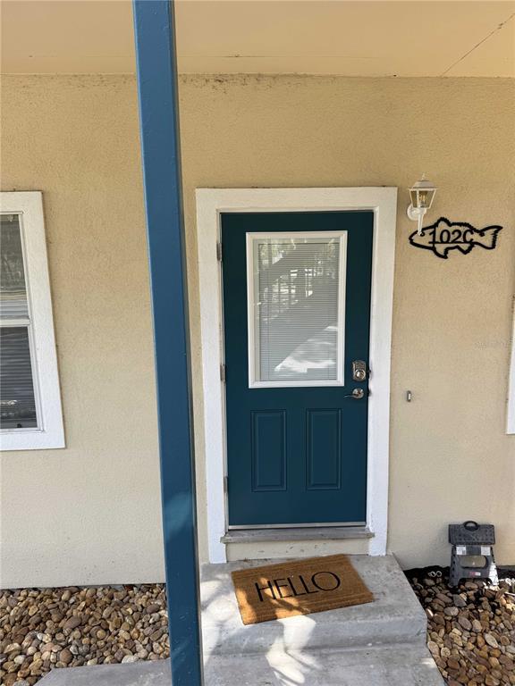 A teal front door with a window and a welcome mat sits on a concrete porch — 30 SE VALARE LANE UNIT 102C, CRYSTAL RIVER, FL