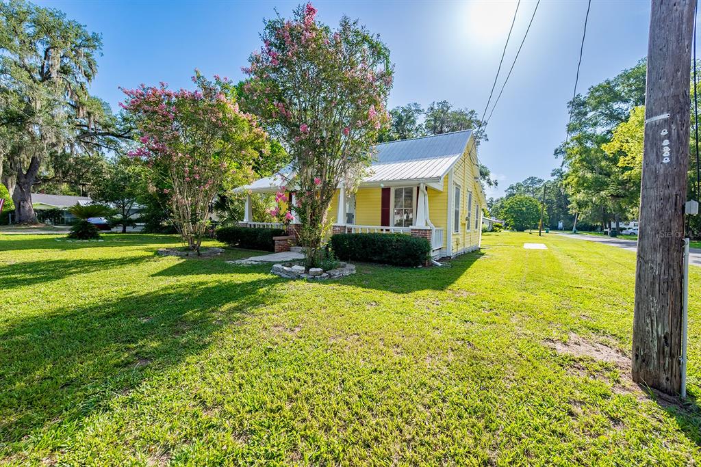 A yellow house with a metal roof sits on a grassy lot with flowering trees — 404 NE 2ND STREET, TRENTON, FL