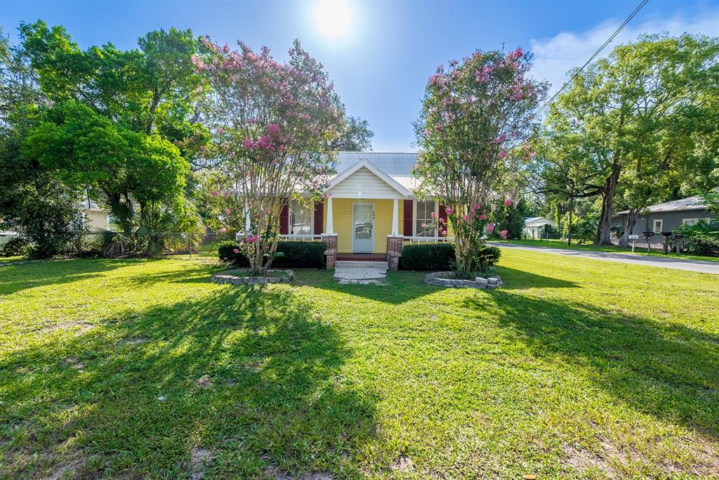A yellow house with a front porch and two blooming crape myrtle trees — 404 NE 2ND STREET, TRENTON, FL