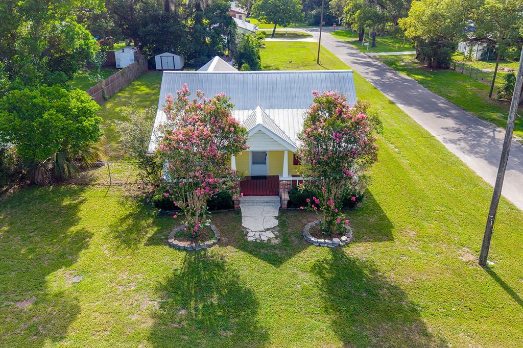 An aerial view shows a yellow cottage with a metal roof and two flowering trees — 404 NE 2ND STREET, TRENTON, FL
