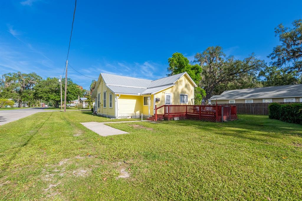 A yellow house with a metal roof and a red wooden deck sits on grass — 404 NE 2ND STREET, TRENTON, FL
