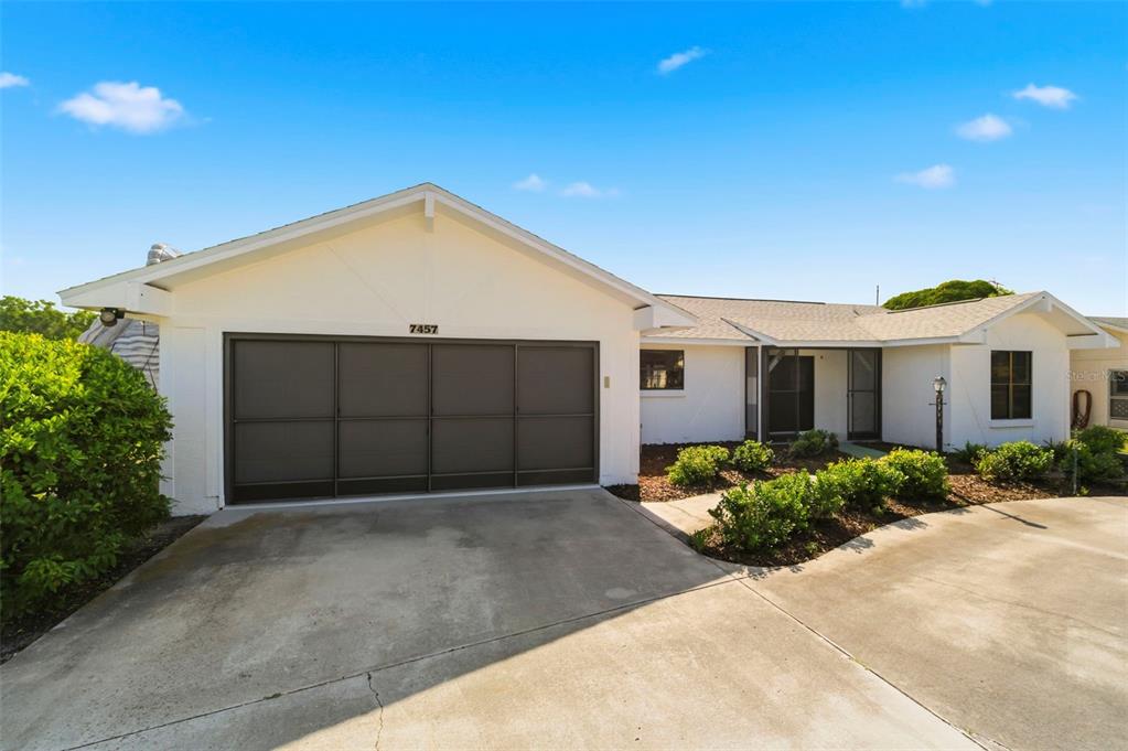 A white single-story house features a dark garage door and a concrete driveway — 7457 GALLOWAY ROAD, WEEKI WACHEE, FL