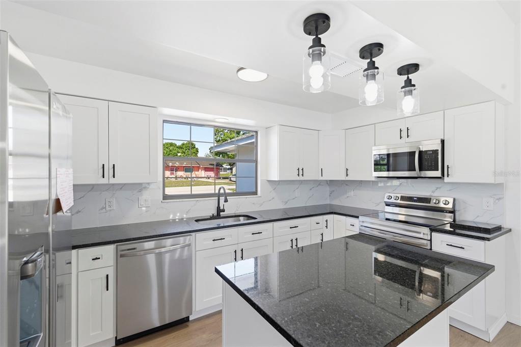 A modern kitchen features white cabinets, black granite countertops, stainless steel appliances, and pendant lighting — 7457 GALLOWAY ROAD, WEEKI WACHEE, FL