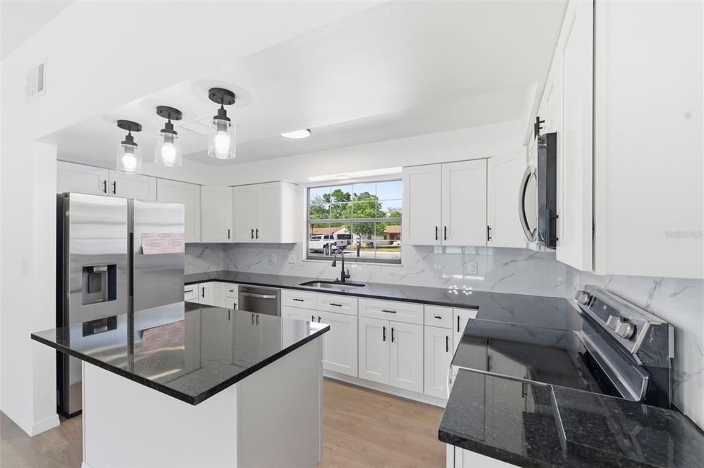 A kitchen with white cabinets, black countertops, stainless steel appliances, and a central island — 7457 GALLOWAY ROAD, WEEKI WACHEE, FL