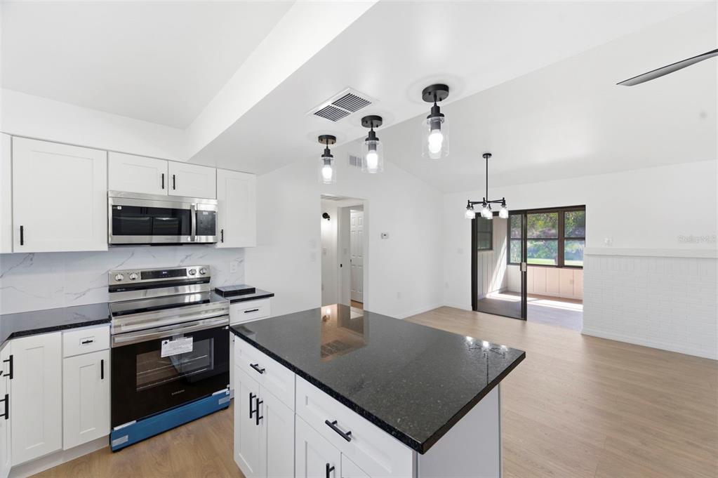 A modern kitchen features white cabinets, black granite countertops, a center island, and stainless appliances — 7457 GALLOWAY ROAD, WEEKI WACHEE, FL