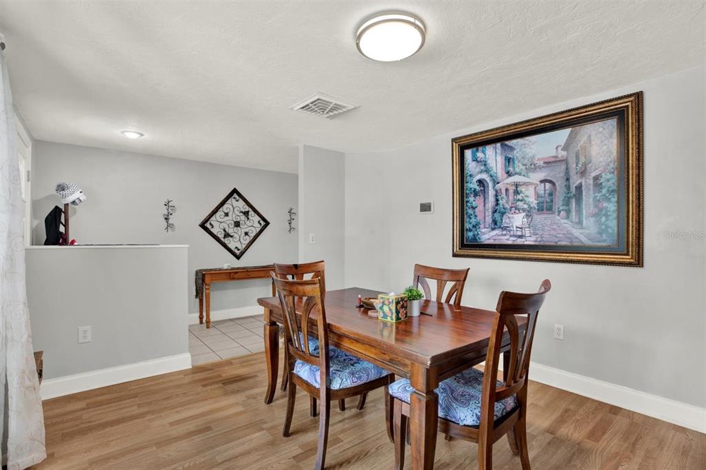 A dining room features a wooden table with four chairs, light flooring, and wall art — 12411 WEATHERSTONE ROW, HUDSON, FL