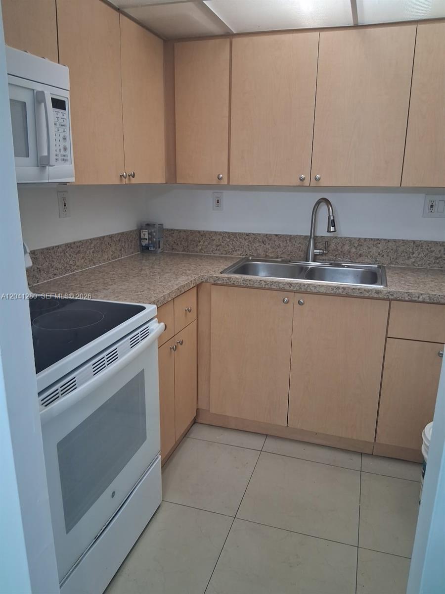 A small kitchen features light wood cabinets, laminate countertops, and white appliances — 4675 W 18th Ct # 606, Hialeah FL 33012, HIALEAH, FL