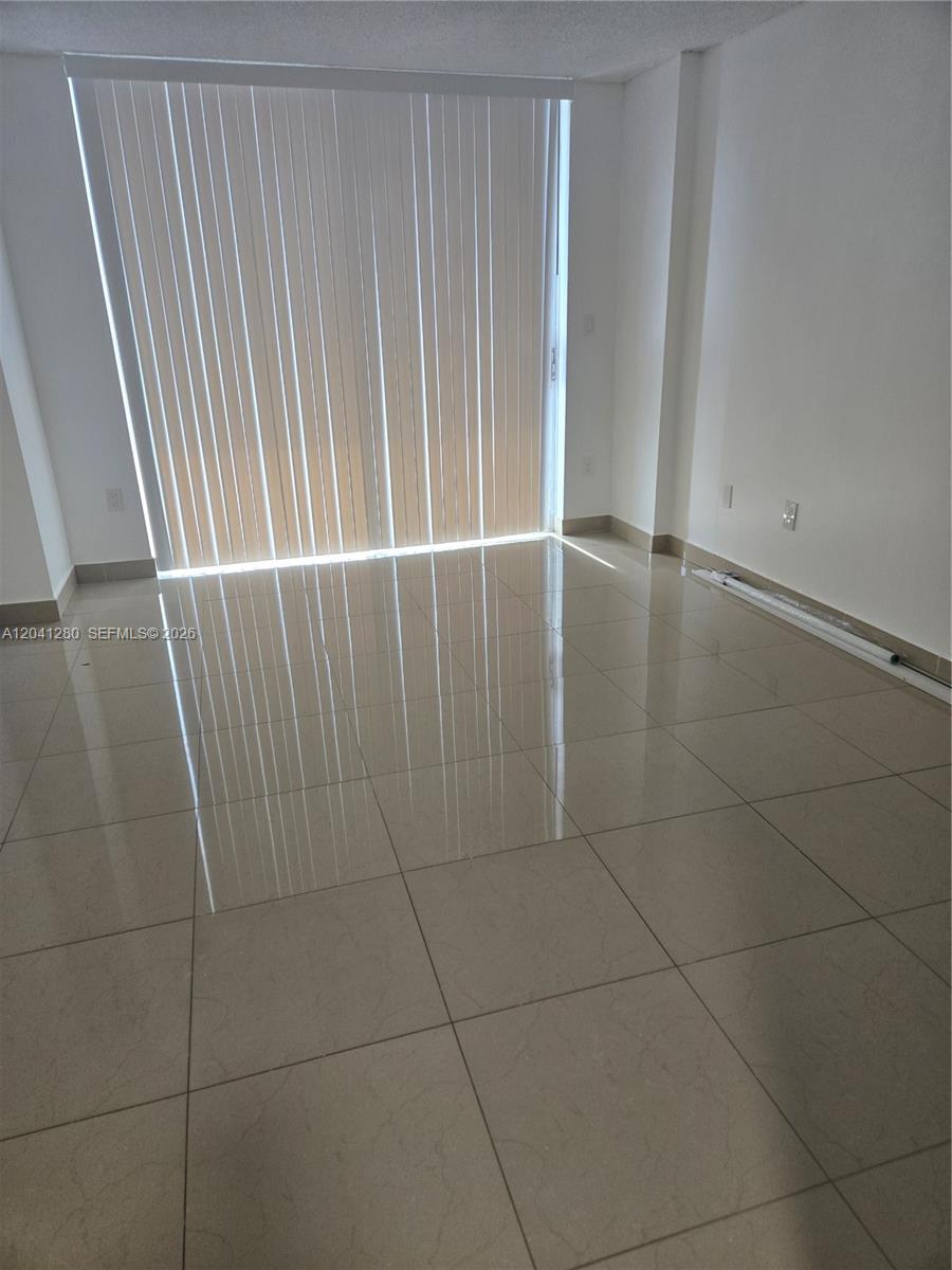 An empty room features light-colored tile flooring and a large sliding glass door with blinds — 4675 W 18th Ct # 606, Hialeah FL 33012, HIALEAH, FL