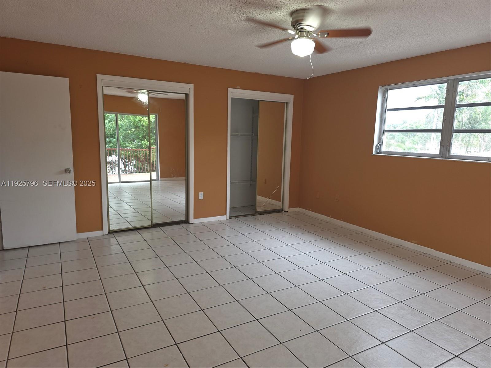 An empty bedroom features orange walls, white tile flooring, a ceiling fan, and mirrored closets — 250 NW 63rd Ct # 2, Miami FL 33126, MIAMI, FL