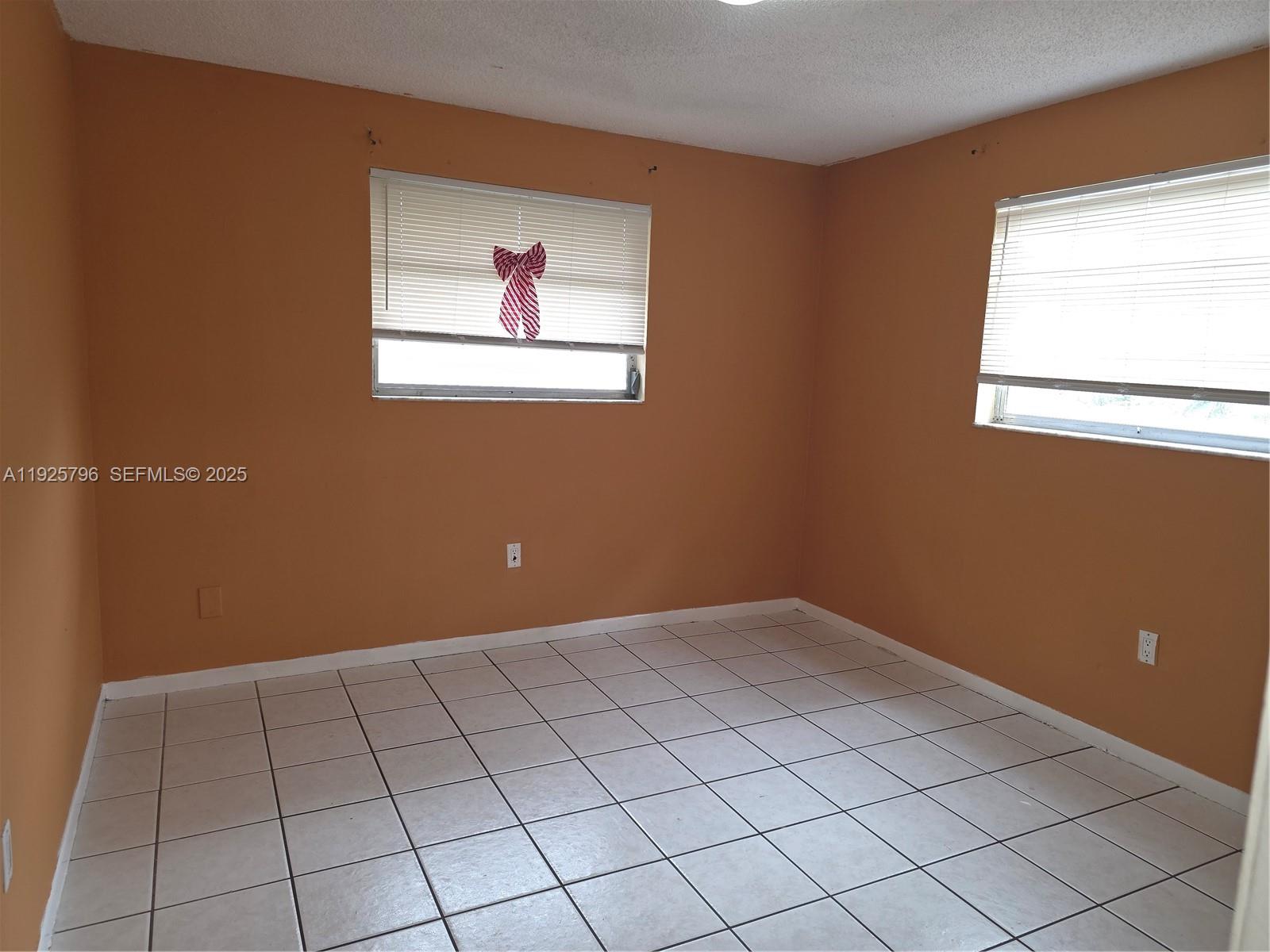 An empty room features orange walls, white tile flooring, and two windows with blinds — 250 NW 63rd Ct # 2, Miami FL 33126, MIAMI, FL