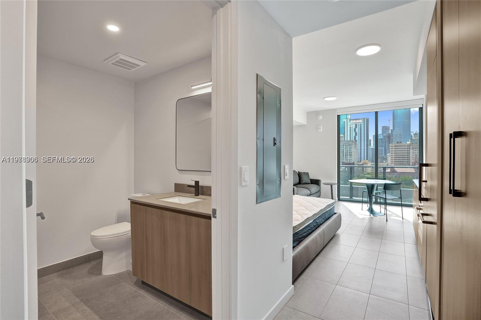 A modern bathroom with a wood vanity opens into a studio apartment with city views — 121 NE 5TH # 801b, Miami FL 33132, MIAMI, FL
