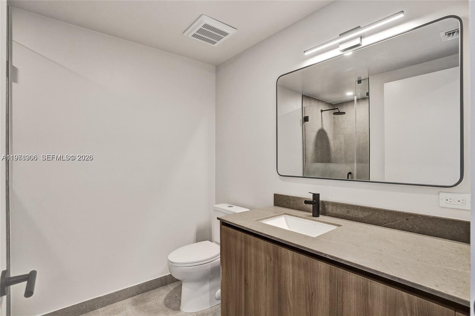 A modern bathroom features a wood vanity, stone countertop, black faucet, and a large mirror — 121 NE 5TH # 801b, Miami FL 33132, MIAMI, FL