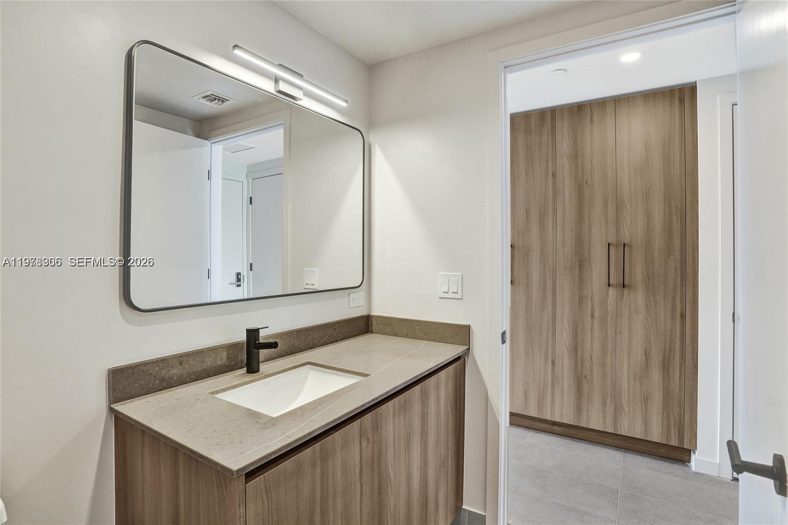 A modern bathroom features a wood vanity, stone countertop, black faucet, and a large mirror — 121 NE 5TH # 801b, Miami FL 33132, MIAMI, FL
